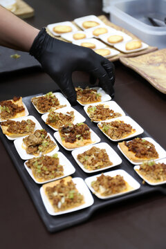 chef preparando con sus manos con guantes, aperitivos de carne en una bandeja para la degustaci&oacute;n y disfrute de los comensales 