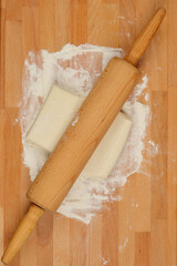  A wooden rolling pin lies across a floured wooden surface with a small rectangle of puff pastry dough in the center