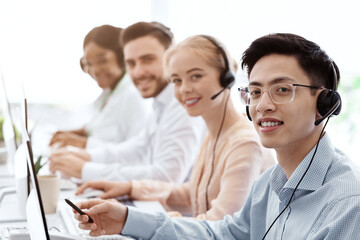 Smiling call center workers sitting in row near their computers at light office, empty space