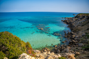 Fototapeta premium Coastline with a sandy beach and rocky shores near the northeasternmost cape of Northern Cyprus. Crystal-clear waters of a blue lagoon and the untouched beauty of the Mediterranean