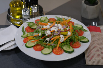 A colorful salad with tomatoes cucumbers carrots peppers and a light dressing arranged on a white plate on a grey table