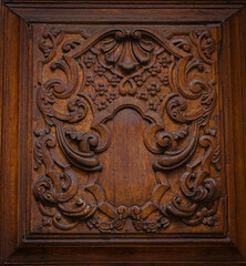 Intricate wood carving on a door panel with a round knob. Decorative design, brown wood, craftsmanship. Vintage style, architectural detail.
