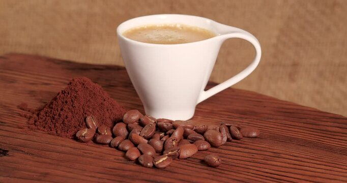 Arabica Coffee Beans Maragogipe on a Wooden and Burlap Background Rotating Video. Elephant Beans with Ground Coffee and White Cup of Hot Espresso Coffee