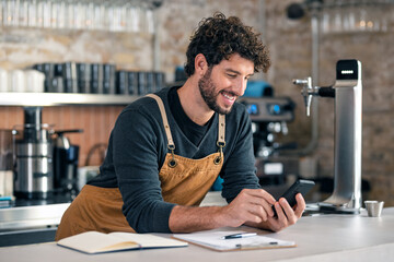 Handsome waiter taking a breakvwhile using smartphone at coffee shop