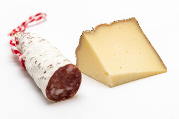a wedge of cured sheep's cheese with a moldy rind and a piece of salami with its cord on a wooden cutting board on a white background