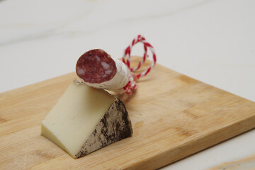 a wedge of cured sheep's cheese with a moldy rind and a piece of salami with its cord on a wooden...