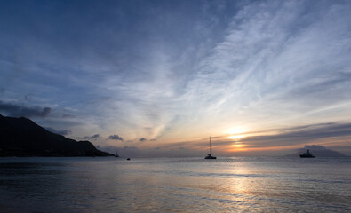 Serene scenery of a calm ocean during sunset, featuring anchored boats
