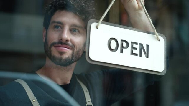 Video of handsome young waiter hanging the open sign on a glass door in the pastry shop