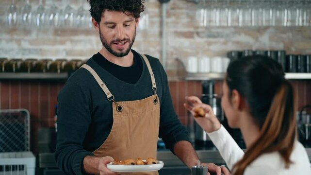 Video of handsome waiter talking with a client while serving chocolate croissants in the pastry shop.