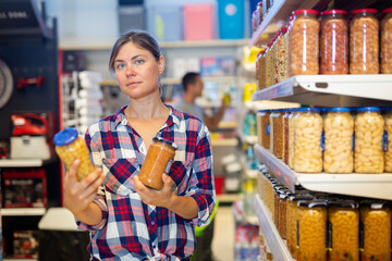 Positive female customer holding glass jar of beans in the supermarket