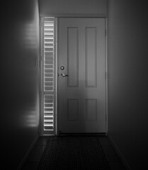 Dark hallway leads to a front door as seen from the inside of a house with copy space in black and white