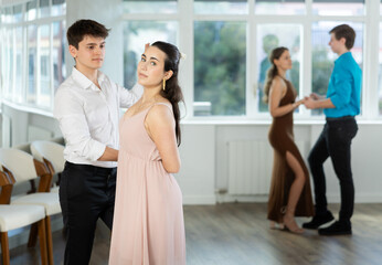 Fototapeta premium Stylish emotional hispanic guy in white shirt and black trousers enjoying impassioned merengue with young female partner wearing elegant dress in latin dance class. Amateur dancing concept..