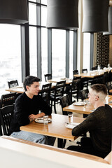A vertical medium shot of a gay men couple on a date in a cozy cafe
A mid shot of a LGBTQ+ couple on a romantic date, sitting by a table and talking in an urban cafe interior