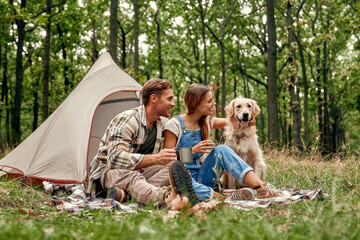 A couple enjoying a delightful camping experience with their dog in a gorgeous forest setting