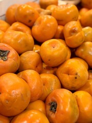 A pile of ripe juicy orange flat persimmons in a box, offered for sale at a supermarket vegetable stand, demonstrates organic, vegetarian and healthy food. Close-up