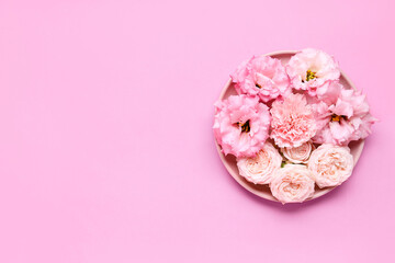 Plate with beautiful flowers on pink background