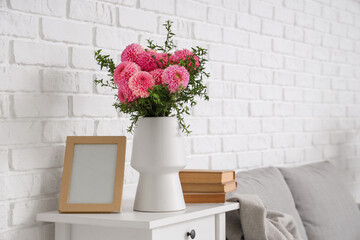 Vase of beautiful pink dahlias with books and frame on bedside table in living room