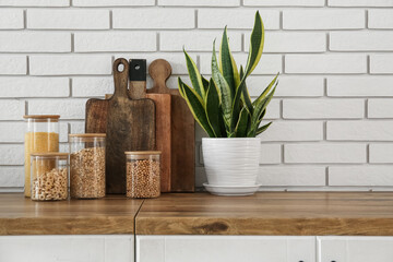 Jars with food, cutting boards and houseplant on wooden countertop in kitchen, closeup
