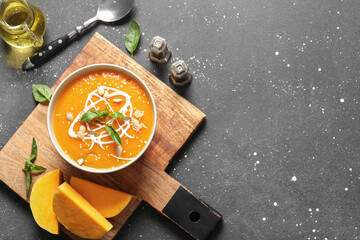 Bowl of delicious pumpkin cream soup with basil and seeds on black background