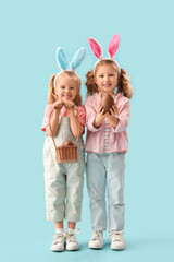 Cute little girls in bunny ears with chocolate Easter eggs on blue background