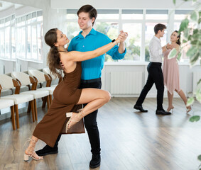 Fototapeta premium Couples in evening dresses suits enjoys pair dance tango, positively interacting with each other on floor. Dance party , hobby for lovers of active lifestyle