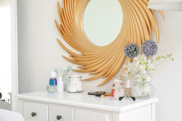 Set of cosmetic products and vase with flowers on table near mirror