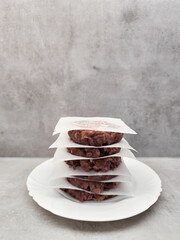 Raw beef burger patties stacked on white plate with baking paper separating them