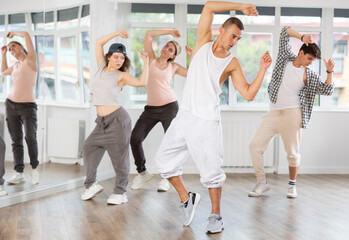 Positive young man engaged in hip-hop together with other attendees of dancing courses for beginners