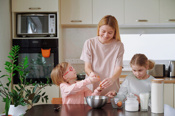 Generational baking moment: mom guides giggling girls in cake preparation, kitchen table cluttered...