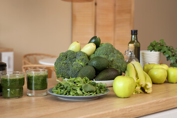 Glasses of healthy green smoothie with different fresh vegetables and fruits on table in kitchen