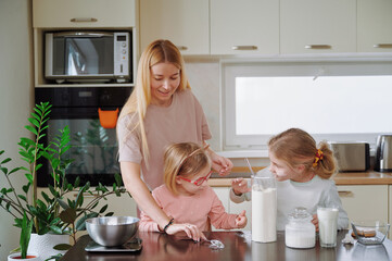 Daughters in pajamas, covered in flour, helping mother with baking in the kitchen