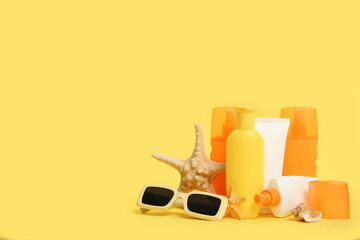Sunglasses, starfishes and bottles of sunscreen cream on yellow background