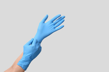 Female doctor putting medical gloves on her hands against grey background