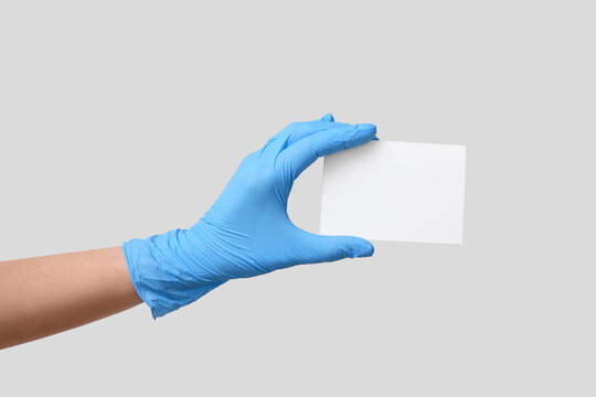 Female hand in medical glove holding blank card on grey background