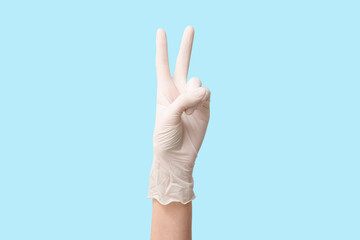 Naklejka premium Female hand in medical glove showing victory gesture on blue background