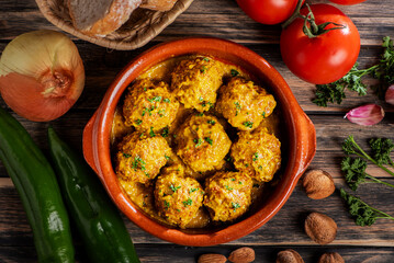Delicious meatballs in almond sauce alongside ingredients for preparation, on a rustic wooden table,top view.