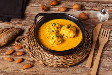 Homemade meatballs in almond sauce in a black bowl on a rustic wooden table, close-up.