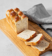 Freshly baked whole grain bread with slices on a wooden board with a napkin on a light background.