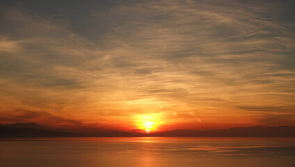 Golden sunset over the Lake Geneva, reflecting warm light on the water and the cloudy sky in Switzerland