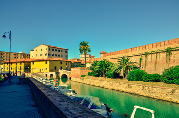 A scenic view of a city canal on a sunny day. The waterway is lined by a historic fortress wall...