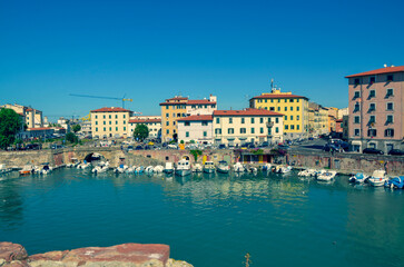 Fototapeta premium A picturesque view of a sun-drenched harbor in a historic European city. Colorful buildings line the turquoise waterway where numerous small boats are moored.