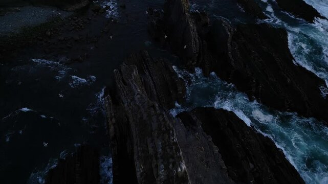 Aerial view of waves crashing against black rocks on the coast