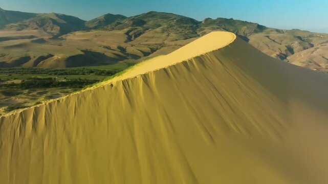 Expansive aerial view of Sarykum Dune, Dagestan, showcasing sunlit dunes with patches of mossy greenery and dynamic cloud formations.