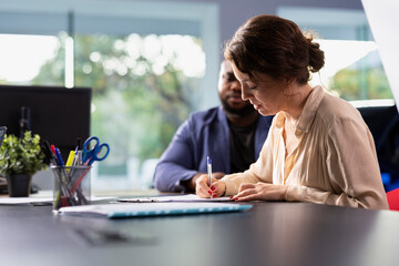 Woman in car dealership signing contract with salesperson after having concerns addressed,...