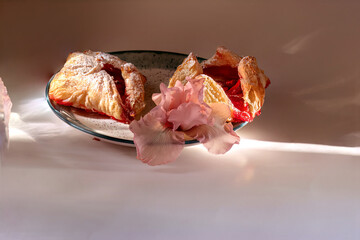 Two puff pastry pies with strawberries on plate decorated with pink iris flower. Fresh homemade baked goods