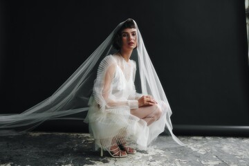 Model wearing a flowing white dress and veil poses in an urban studio during a fashion shoot in natural light
