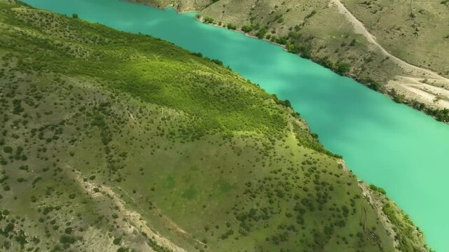 Aerial drone footage of the winding Kazenoyam Lake, Chechnya, featuring lush greenery, cloud shadows, and stunning blue-green mountain waters.