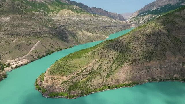 Breathtaking aerial view of Kazenoyam Lake, Chechnya, with its winding shoreline, cloud shadows drifting over the vibrant waters and mountains.