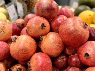 Lots of ripe red pomegranates on a market counter for sale on sale in vegetable stand display at supermarket show organic food, vegetarian food, healthy food. Close-up