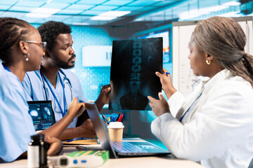 African american general practitioner leading a healthcare team in a cabinet, analyzing MRI imaging...